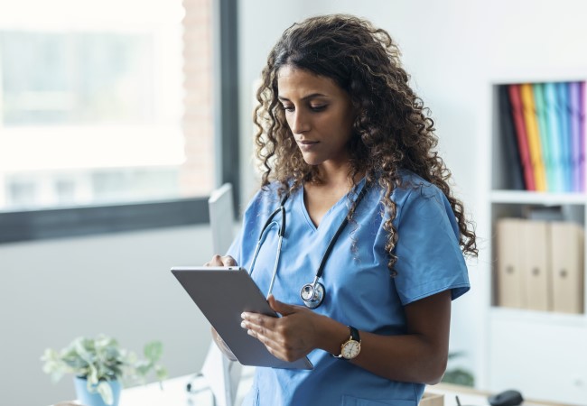 Nurse practitioner working on a tablet in a hospital setting Nurse practitioner working on a tablet in a hospital setting