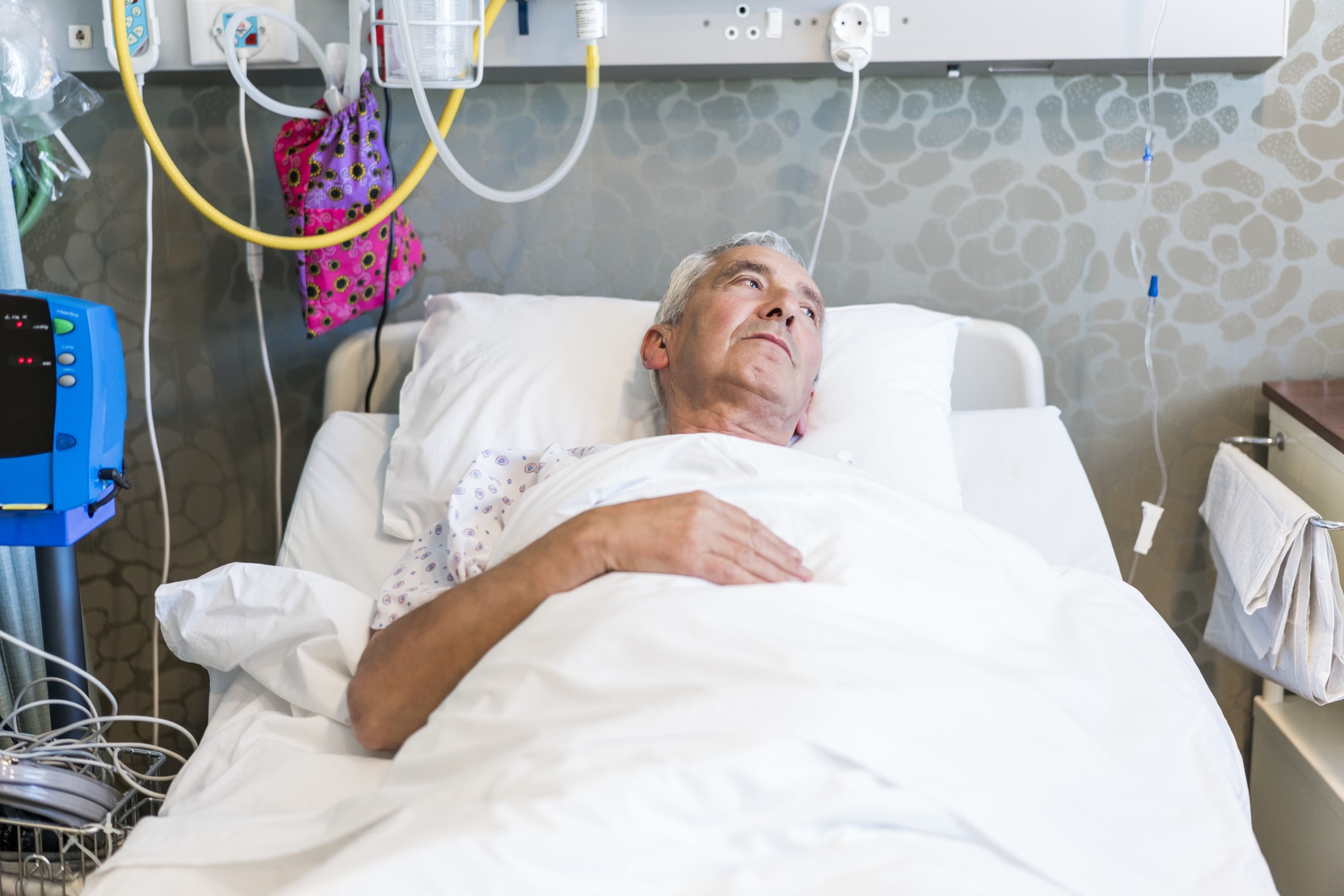 unhappy patient lays in hospital bed, surrounded by  tubes and cords
