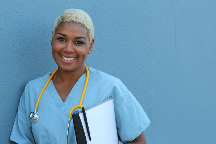smiling nurse in blue scrubs leaning on blue wall