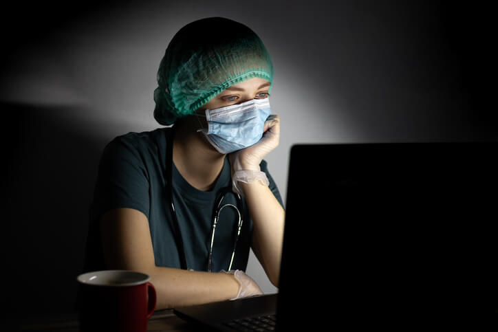 nurse with mask and cap on sitting in light cast only by computer nurse with mask and cap on sitting in light cast only by computer