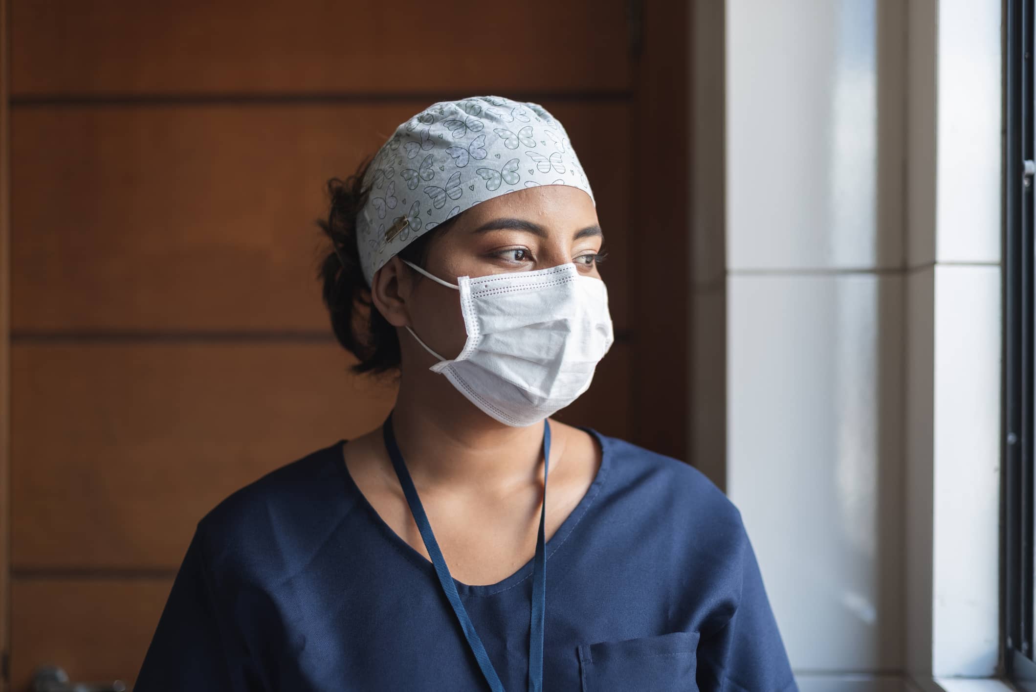 Travel nurse in scrubs and mask gazing out the window